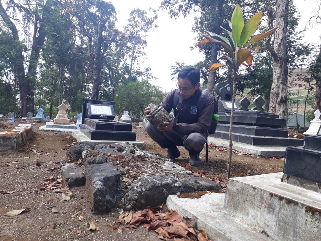 BATUAN CANDI: Salah satu pegiat sejarah dari Komunitas Cagar Budaya Banjarnegara tengah mengamati batu candi yang digunakan untuk nisan makam warga di Desa Dieng Kulon, Kecamatan Batur. (60)